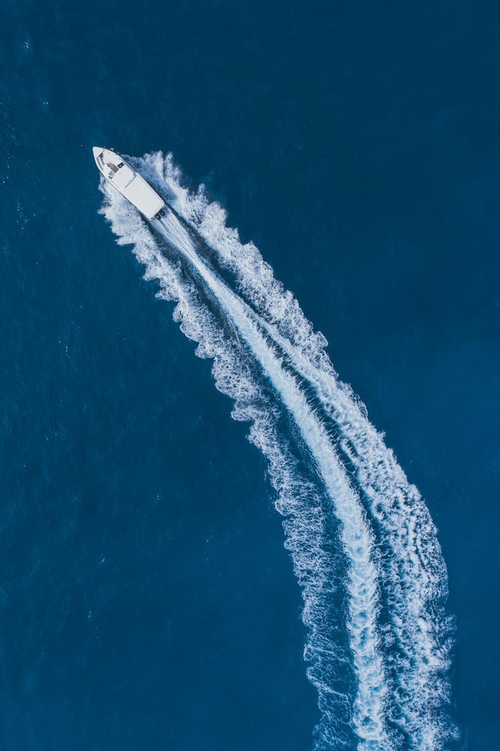 Aerial view of a speedboat carving a white wake across deep blue sea