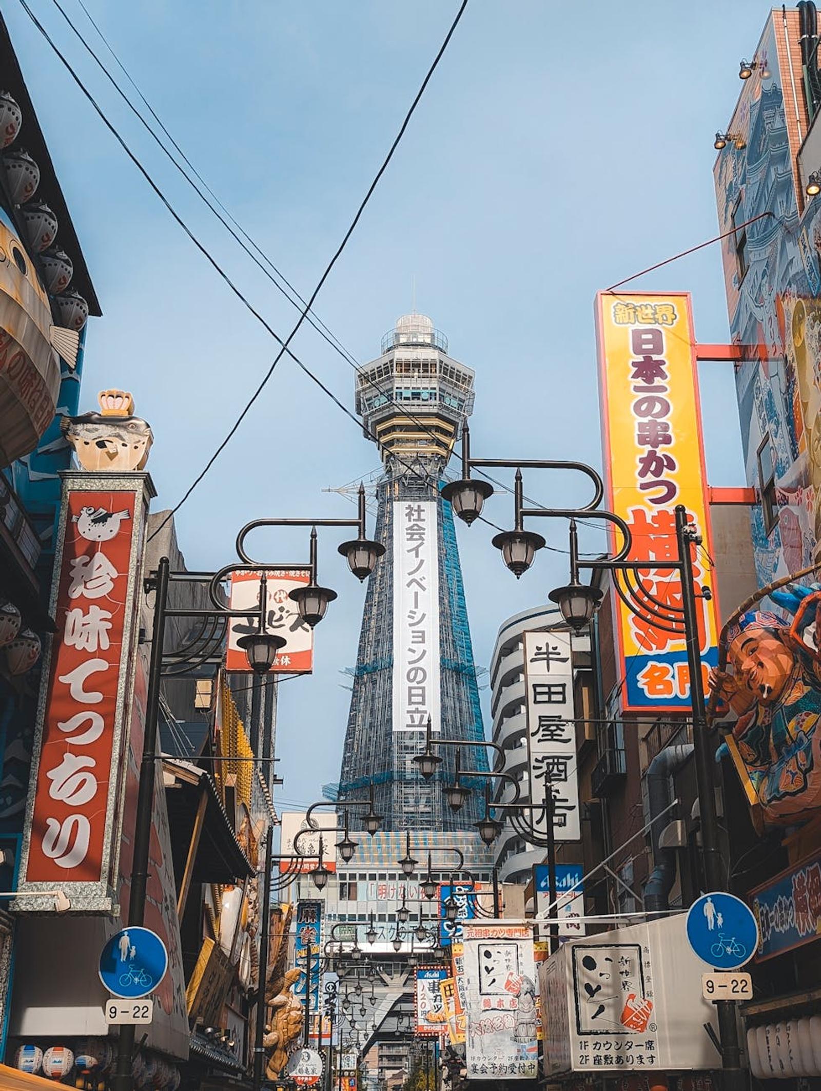 Observation tower rising above a narrow street lined with vibrant signboards