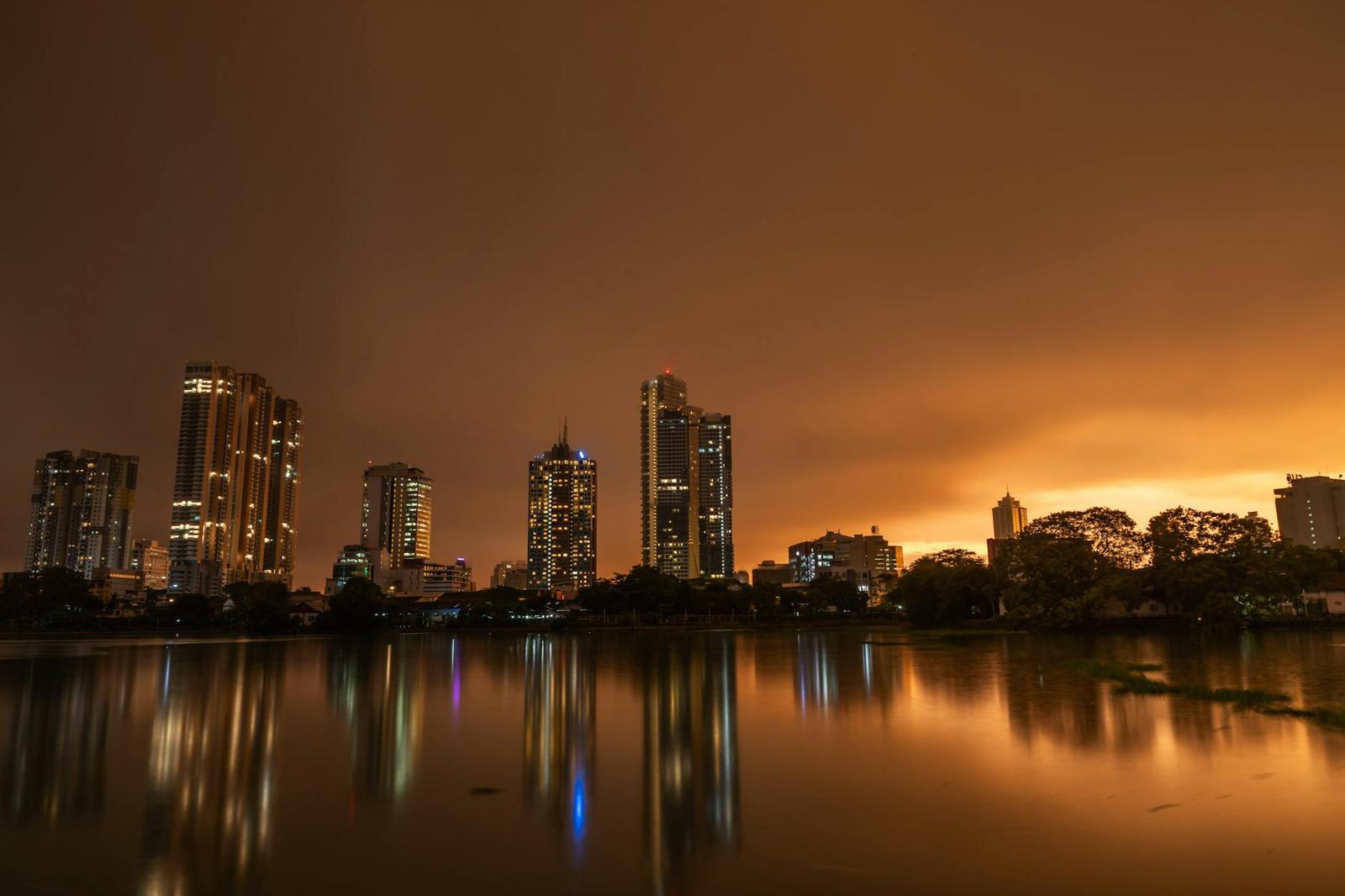 City skyline lights reflected in a still lake under a glowing orange night sky