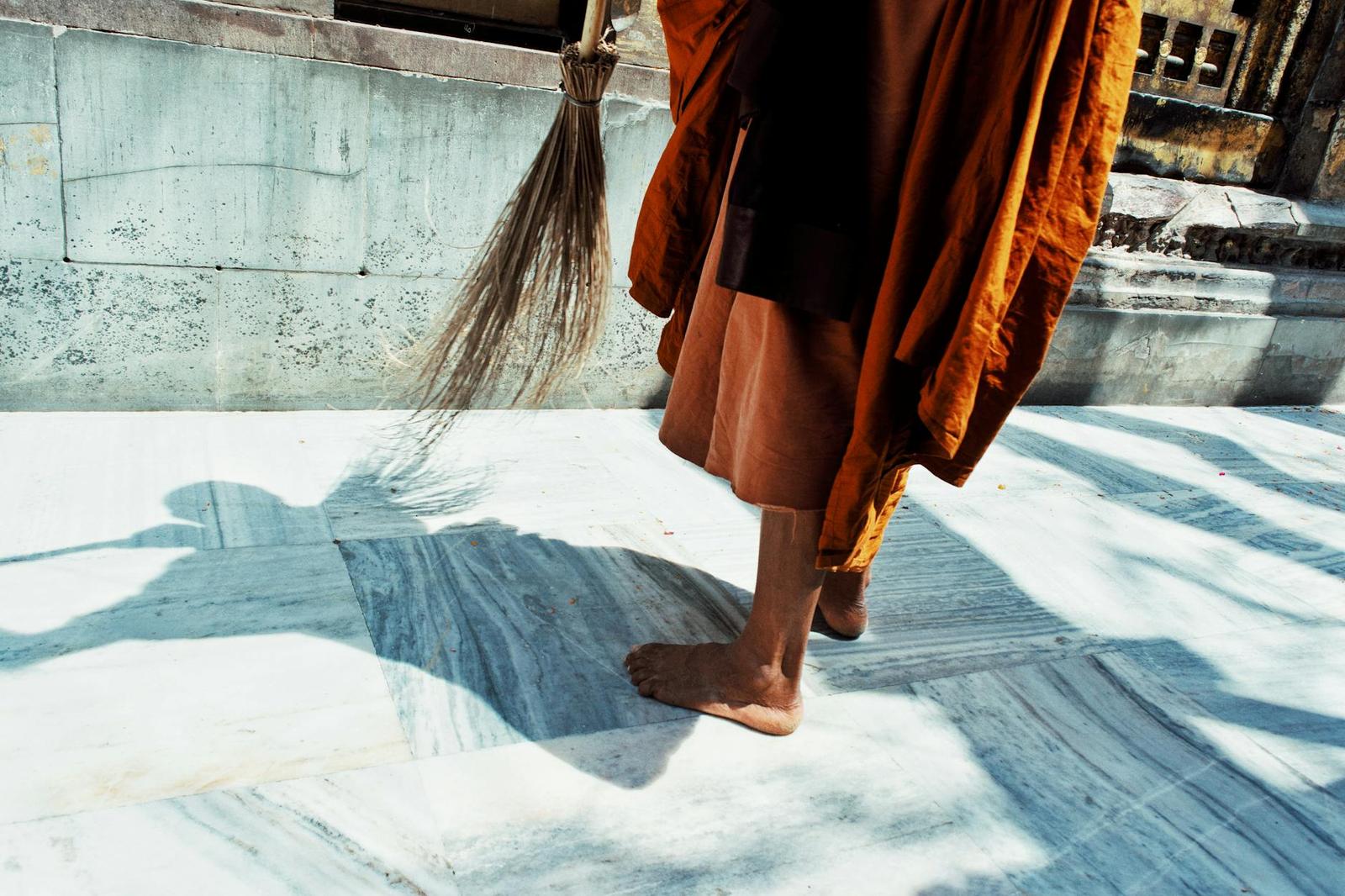 Close-up of a barefoot monk in saffron robes sweeping a marble courtyard