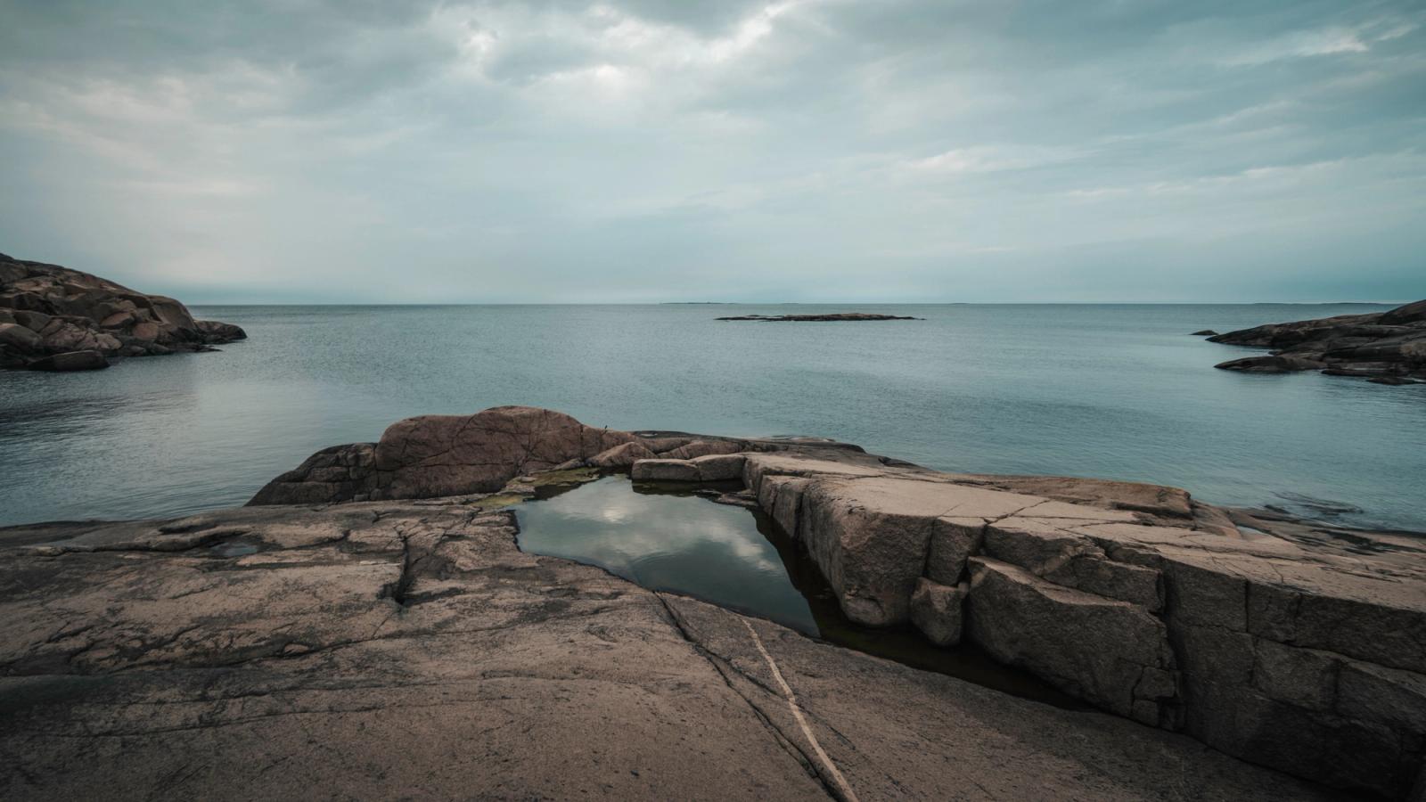 Peaceful coastal landscape with rocky shore and calm sea under cloudy skies