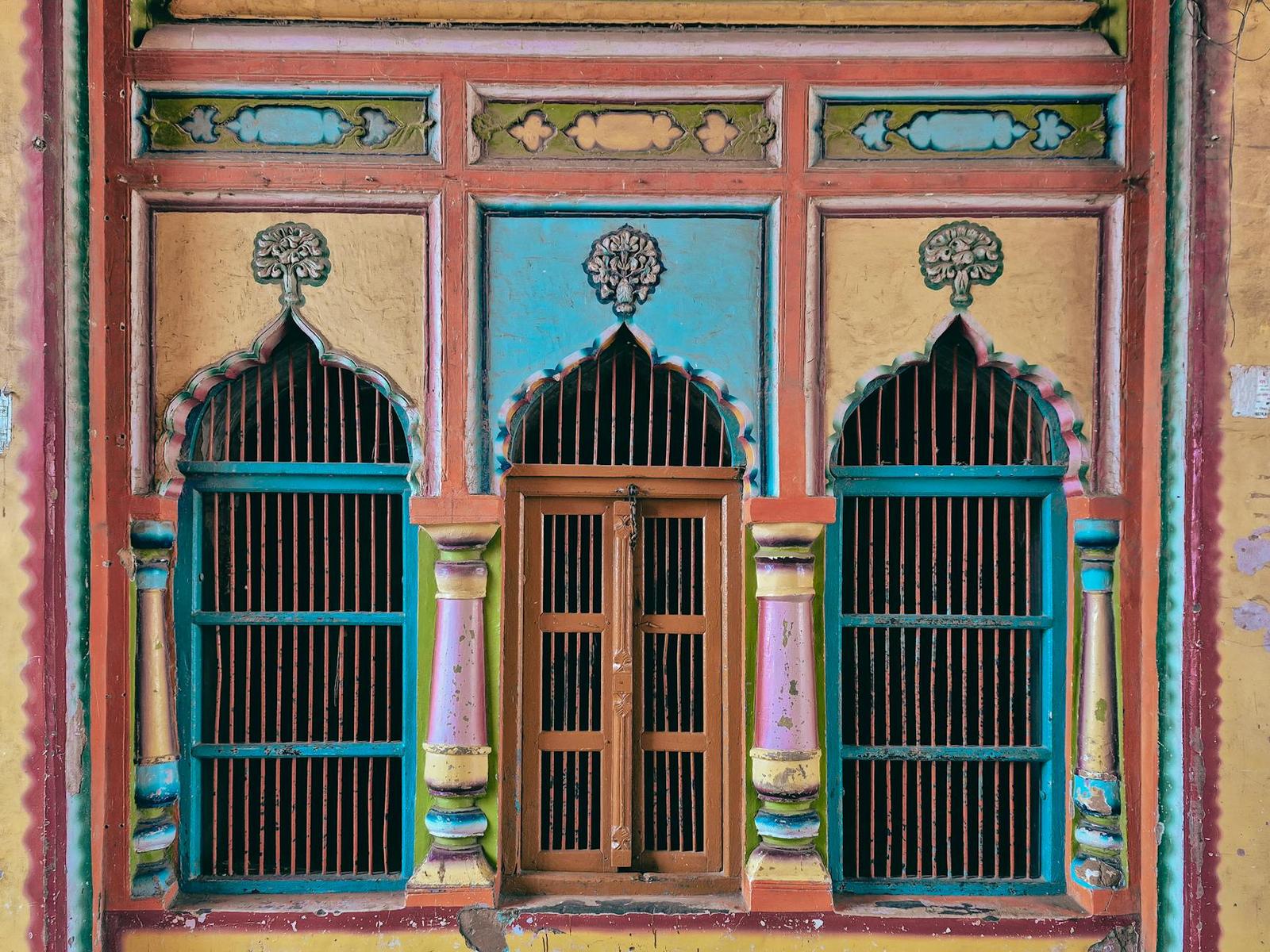 A brightly painted haveli window with arched iron grilles flanking a wooden door