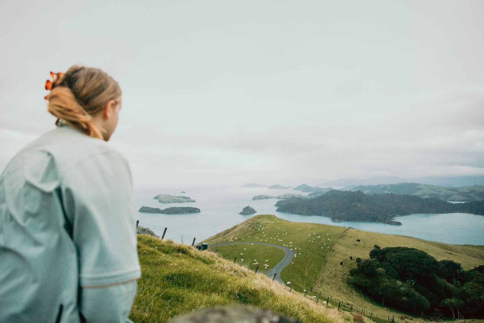 A woman looks out over a green coastal hillside dotted with grazing sheep