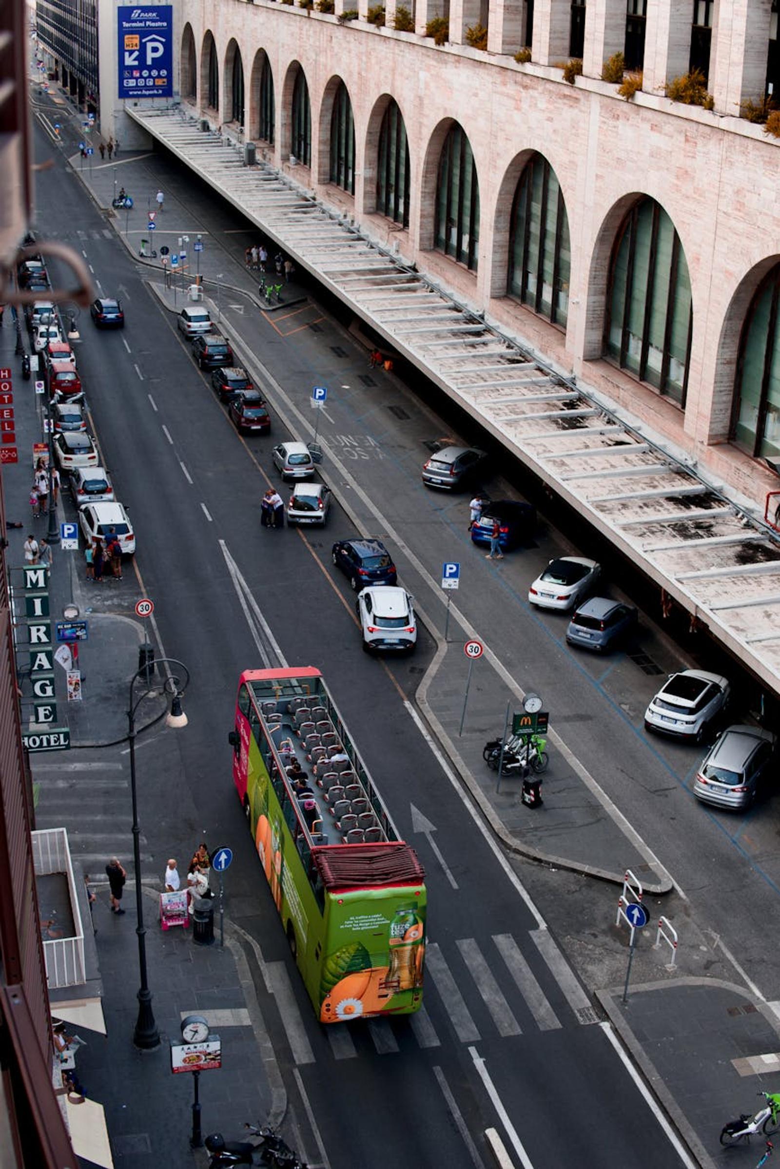 Arcaded building along a city street with a green double-decker tour bus
