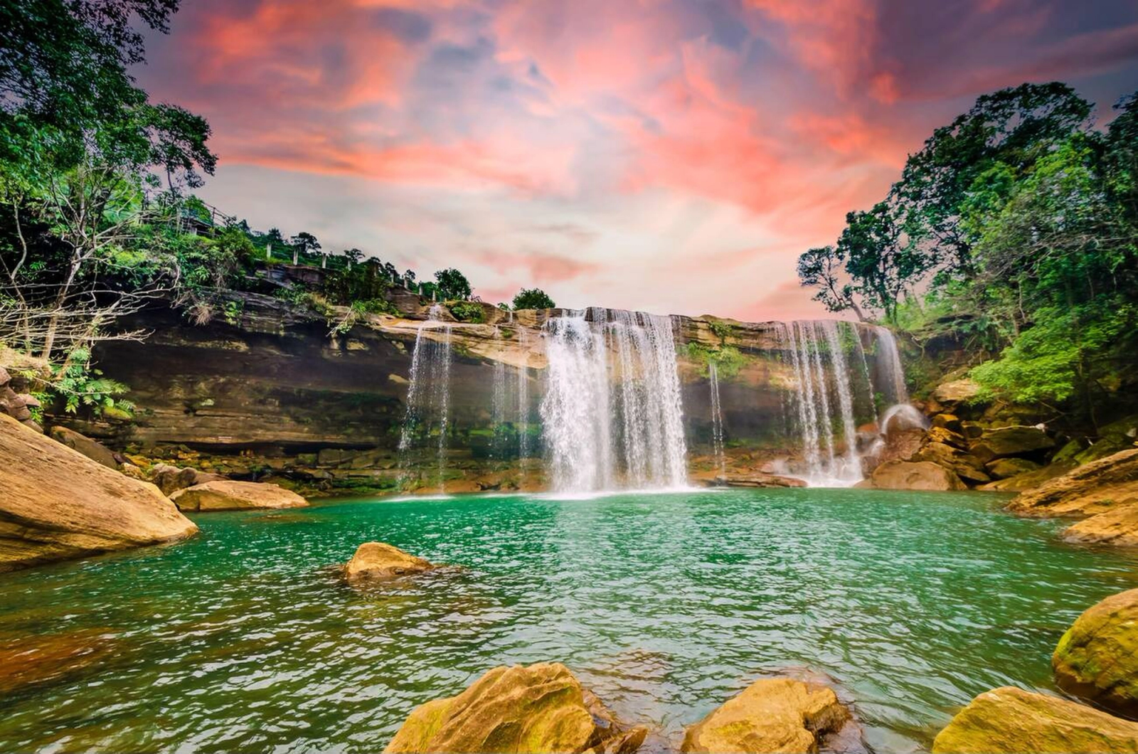 A waterfall cascading into a turquoise pool beneath a pink sunset sky
