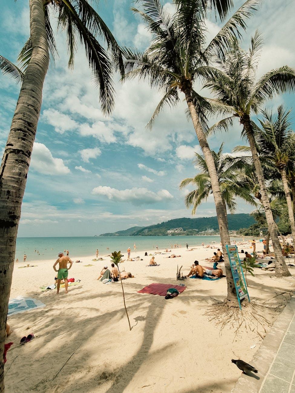 Sunbathers scattered along a busy tropical beach with a swimmer wading in