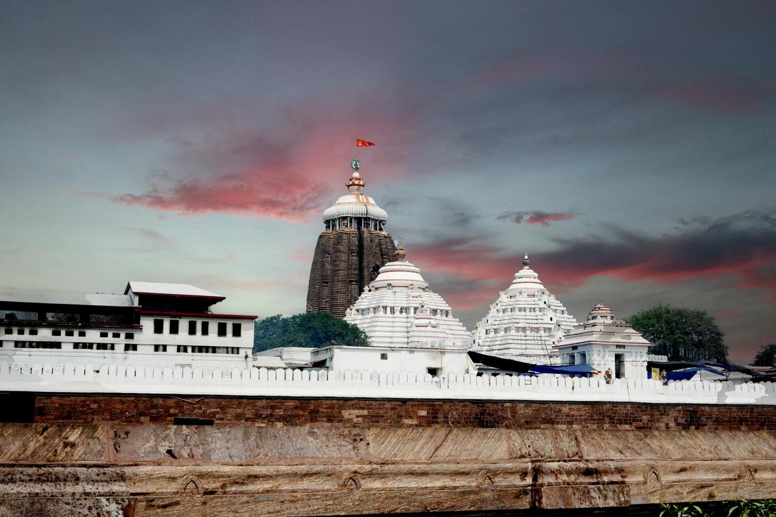 A white temple complex with a dark spire and red flag against a dusky pink sky