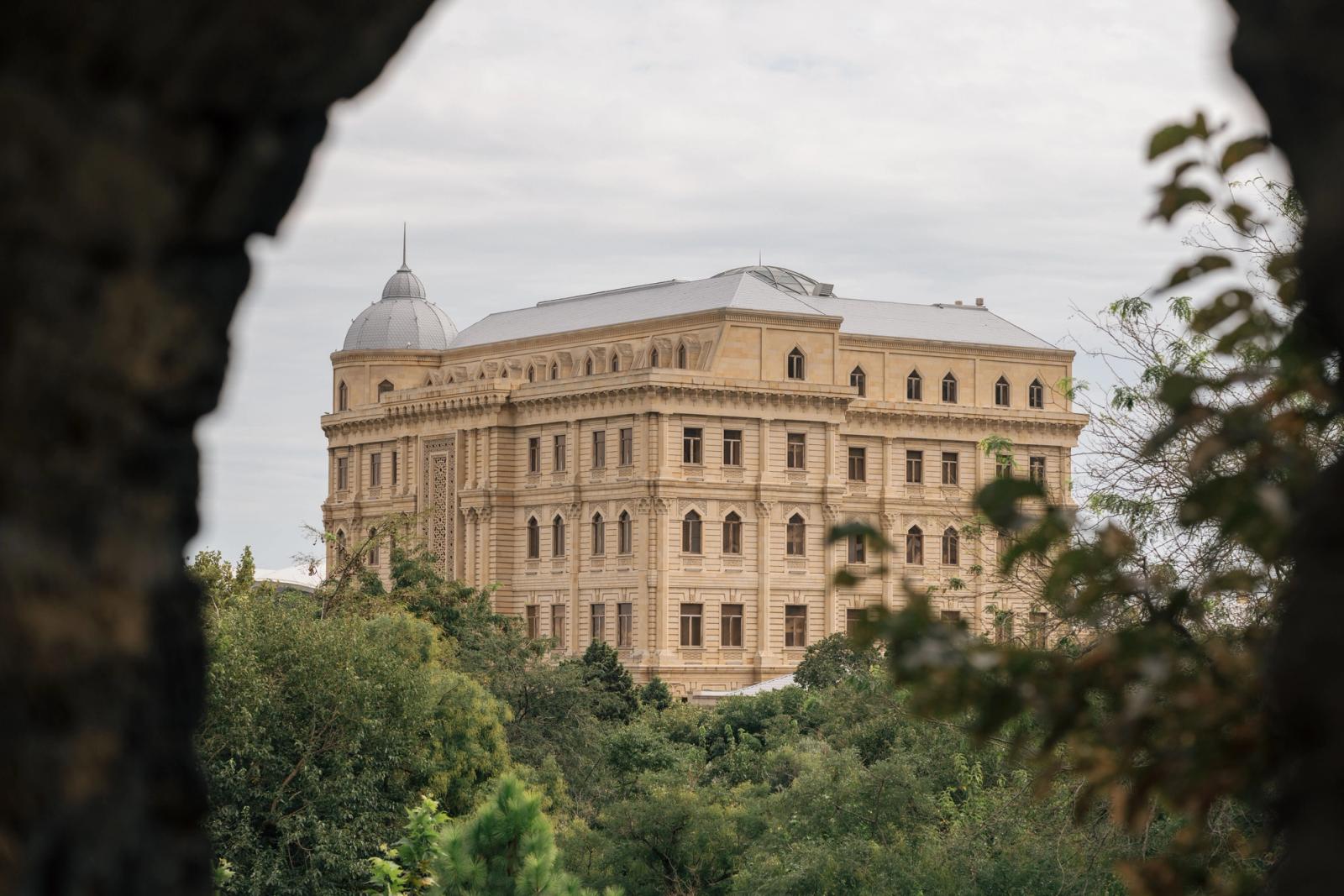 A grand historical building seen through trees in Baku, showcasing neoclassical architecture