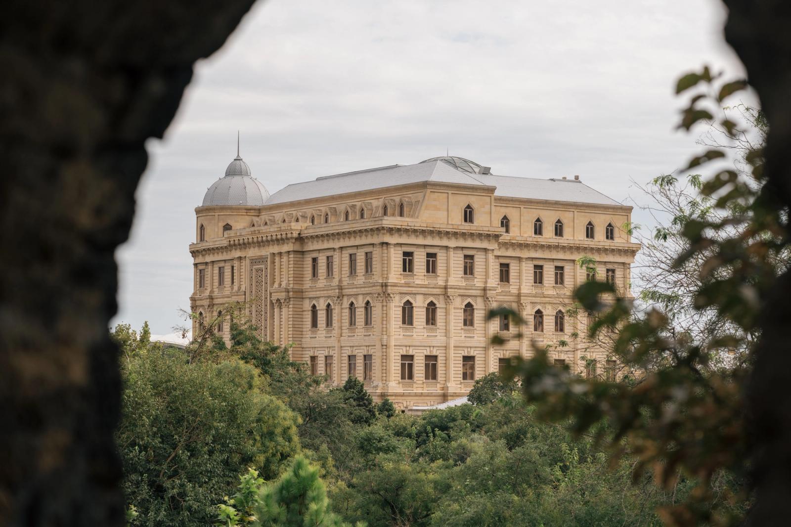 A grand historical building seen through trees in Baku, showcasing neoclassical architecture