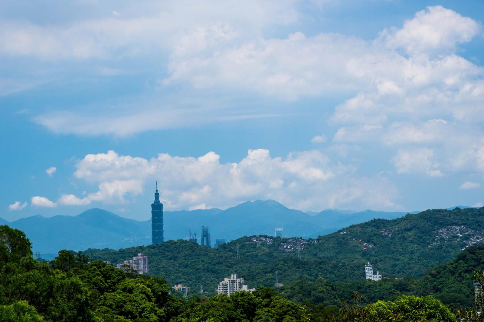 Distant view of Taipei 101 surrounded by verdant mountains and a clear blue sky