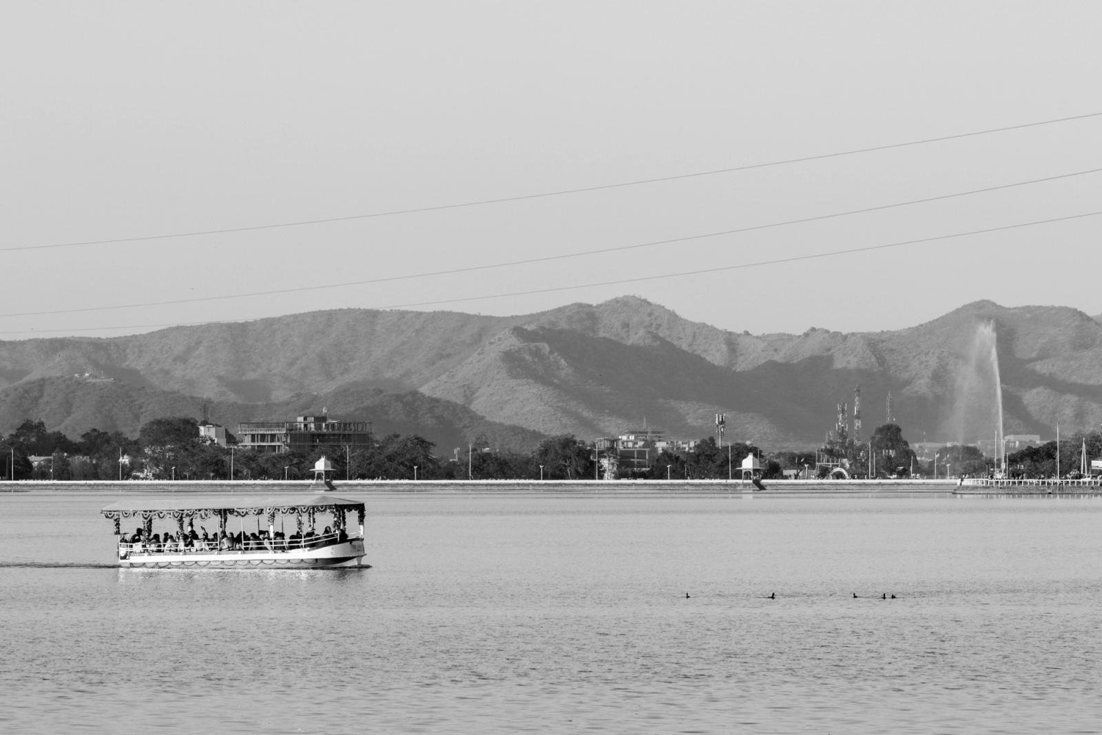 A black and white view of a boat on Lake Pichola with mountains in Udaipur, India