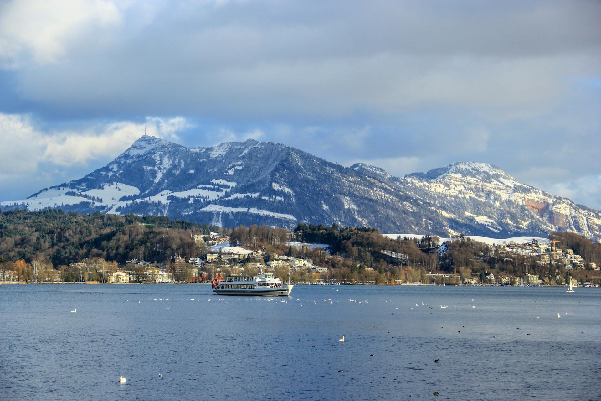 Passenger boat crossing a lake below snow-streaked mountains
