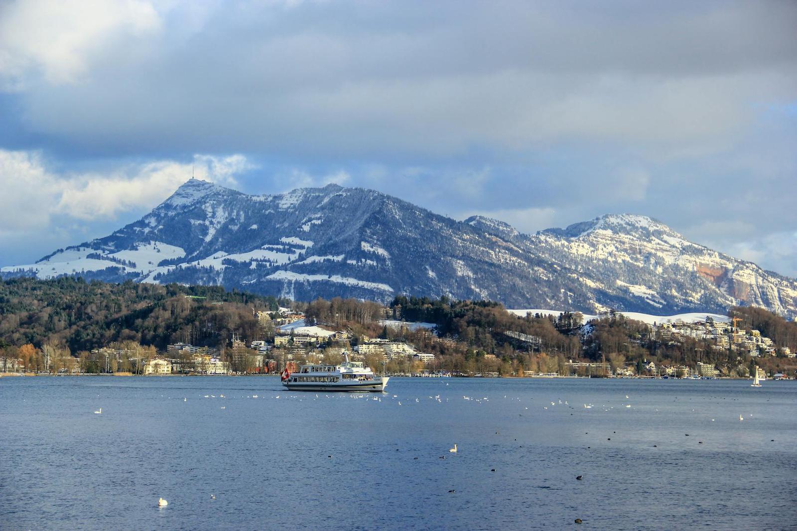 Passenger boat crossing a lake below snow-streaked mountains