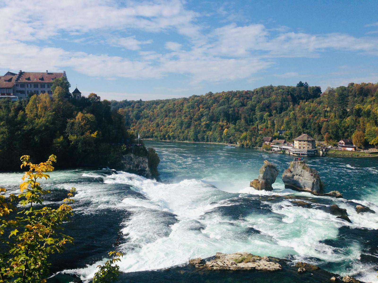 Wide waterfall churning past a cliffside castle and forested banks