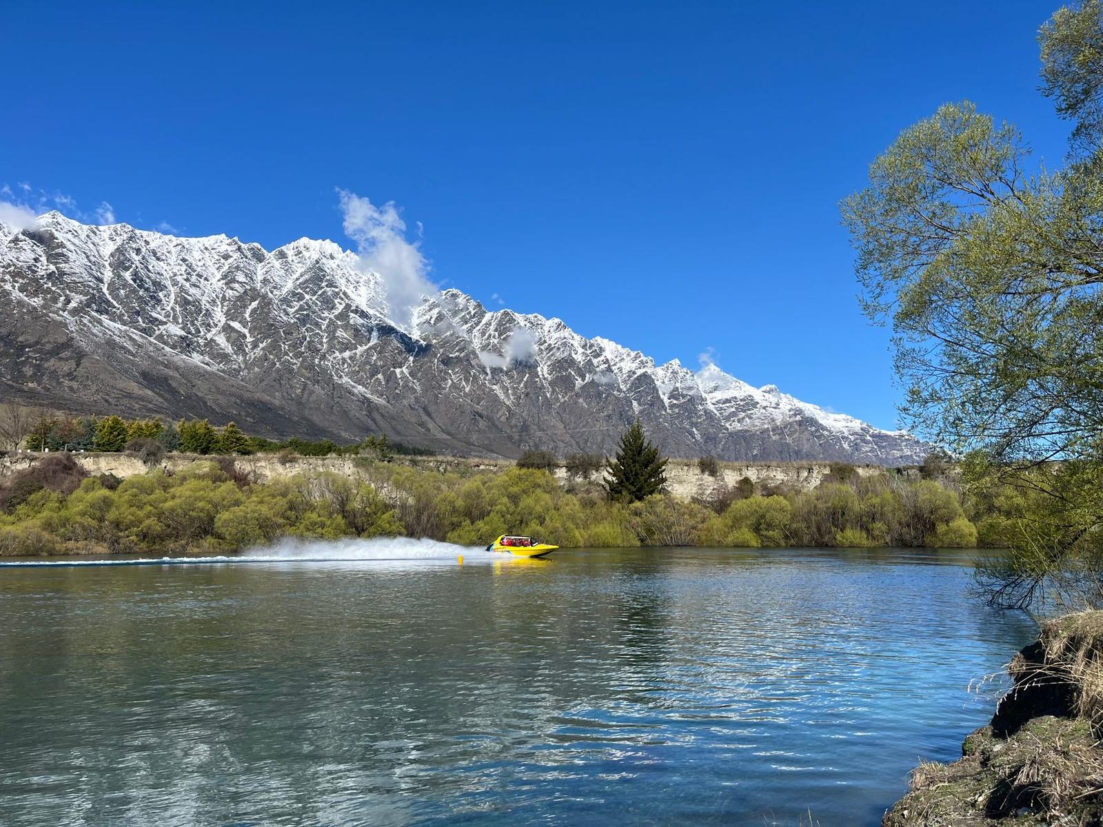 Jet boat speeds across a serene lake with snow-covered mountains in the background