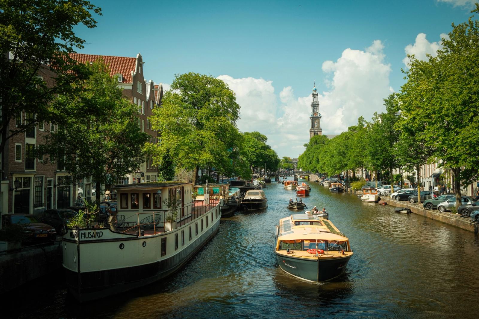 Scenic view of Amsterdam's iconic canal with historic boats and lush greenery under a bright blue sky