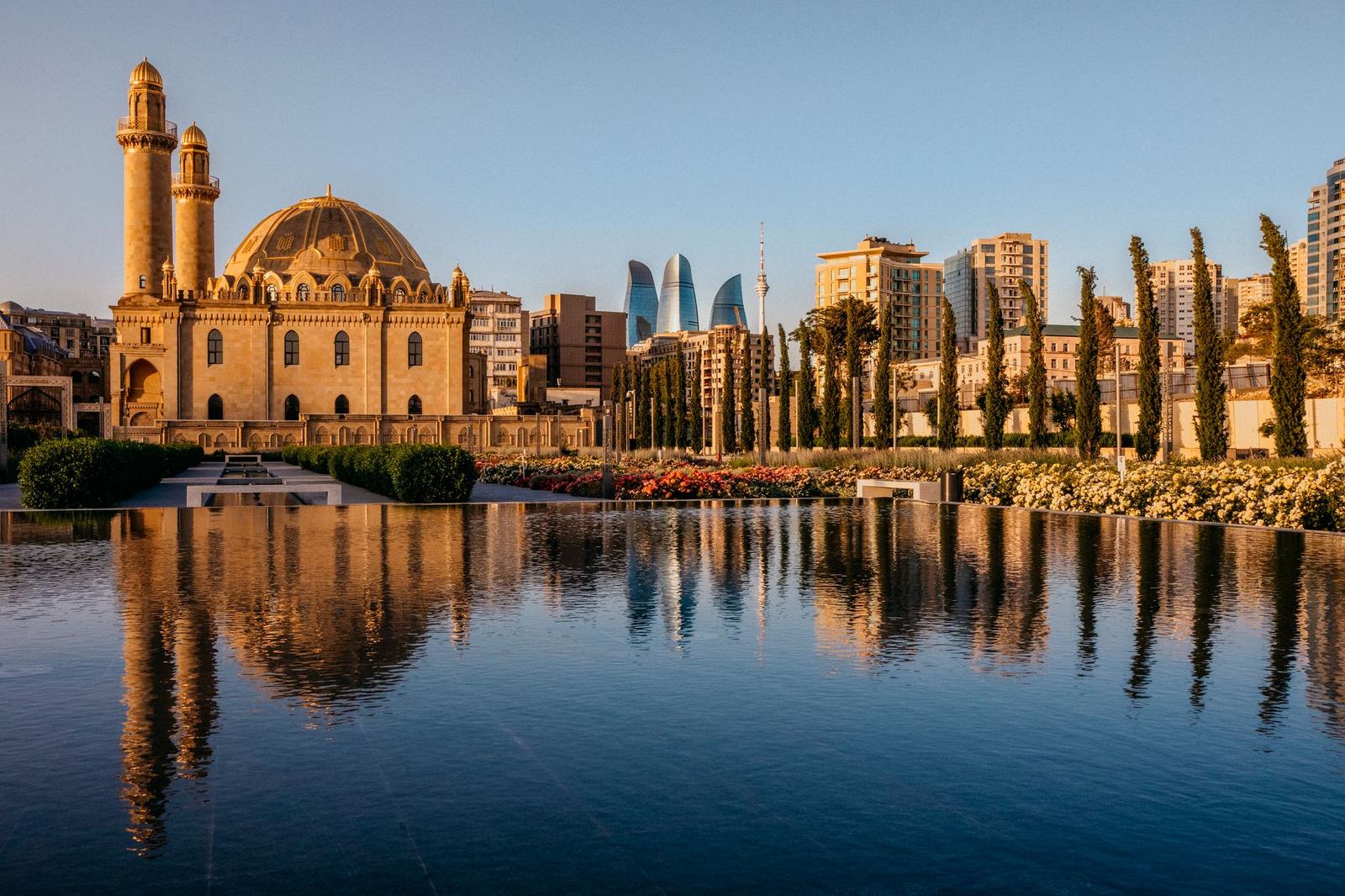 A domed mosque with twin minarets reflected in a still pool before a modern skyline