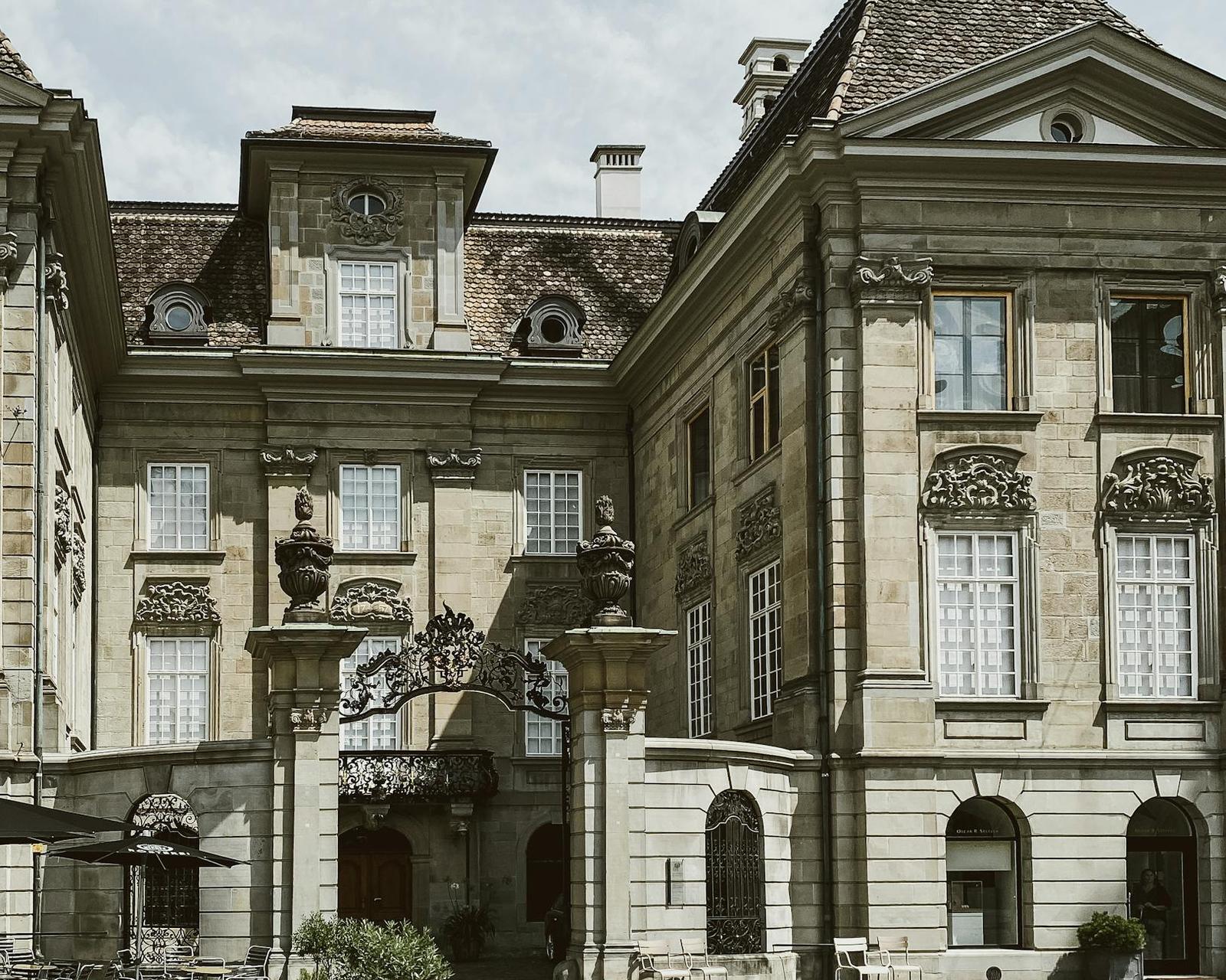 Ornate stone mansion courtyard with an iron gate and umbrella-shaded terrace