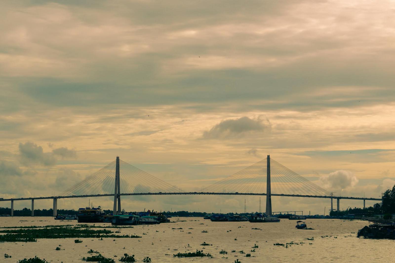 Cable-stayed bridge spanning a wide river under a cloudy sky