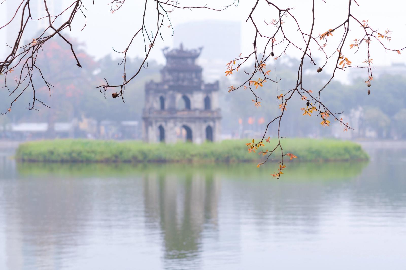 A serene view of Turtle Tower on Hoan Kiem Lake in Hanoi, framed by tree branches