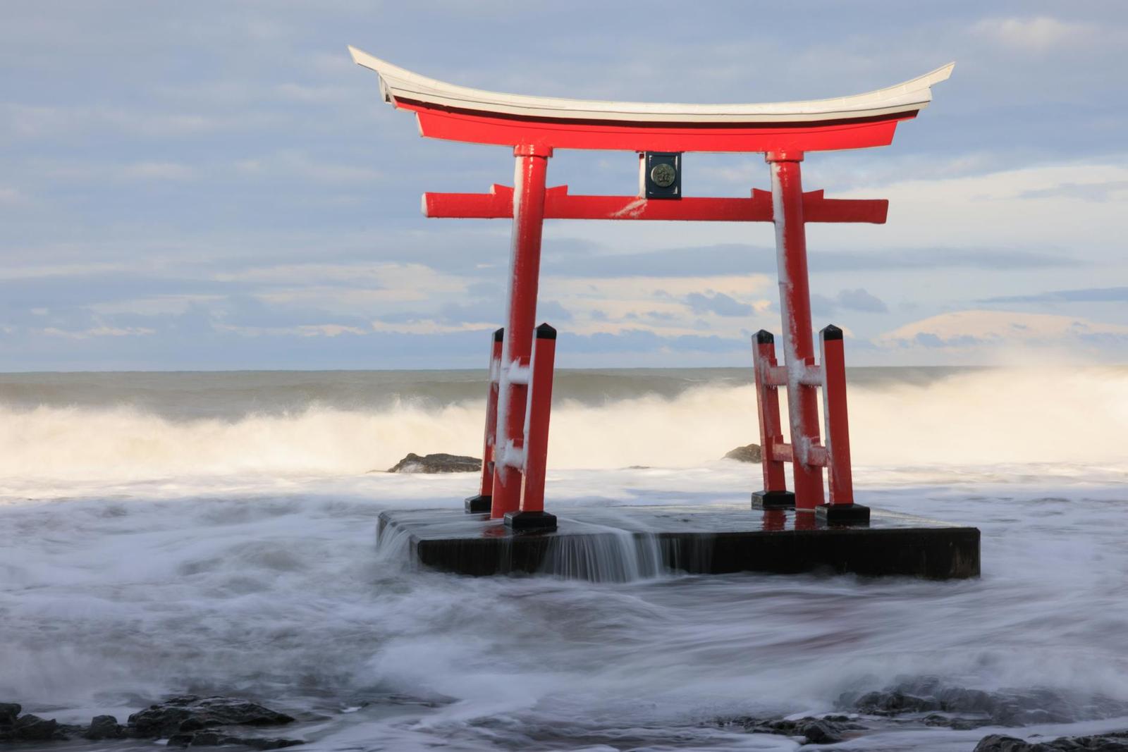 A red torii shrine gate standing in crashing ocean waves