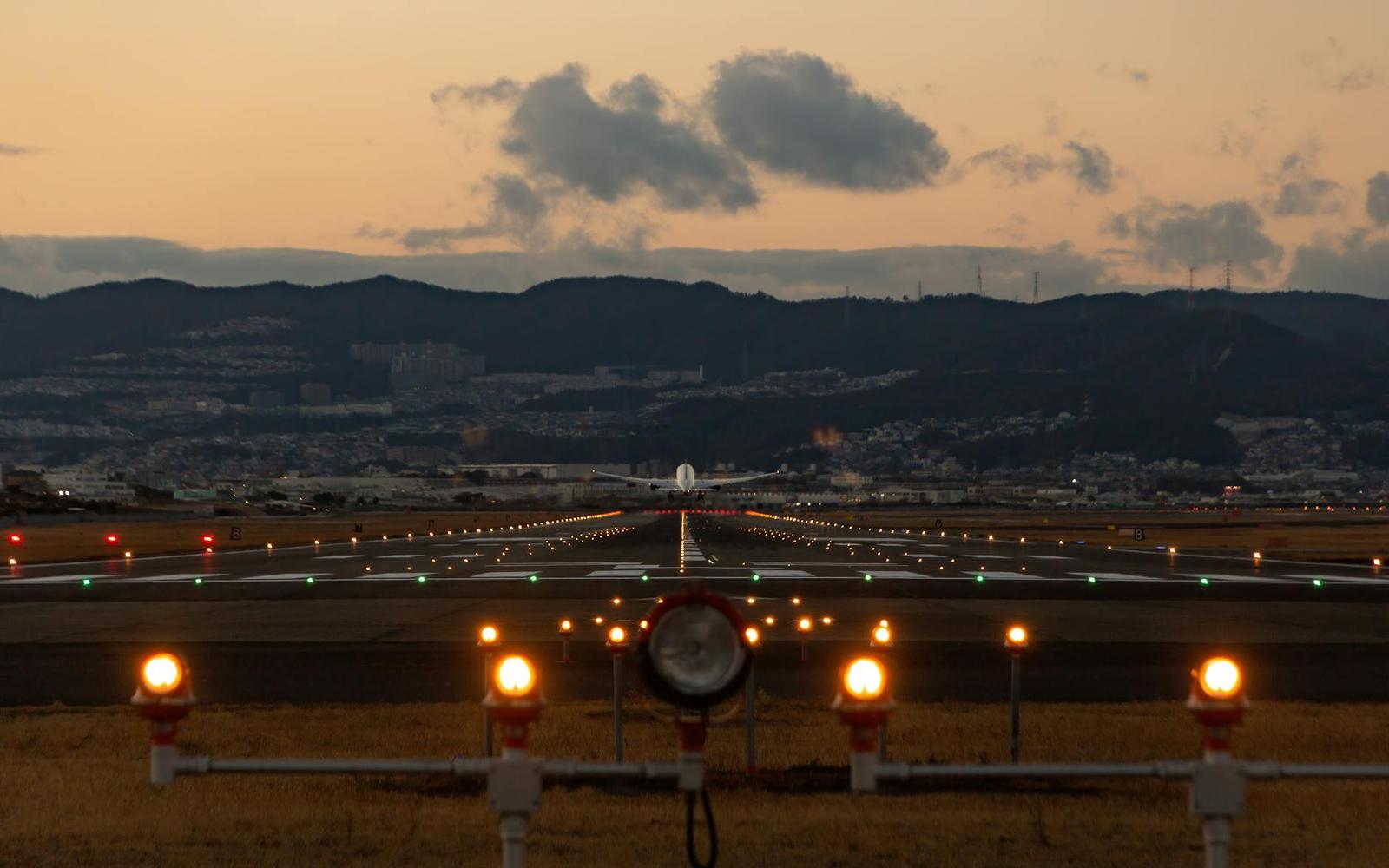 An airport runway lit up at dusk with a plane on approach