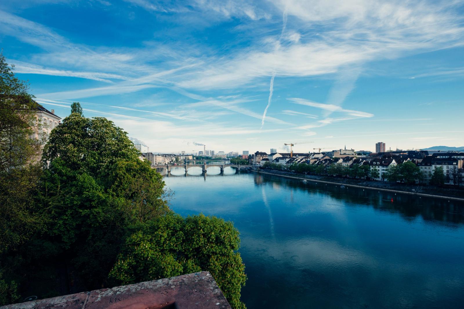 Beautiful view of the Rhine River flowing through Basel, Switzerland, with clear skies and green trees