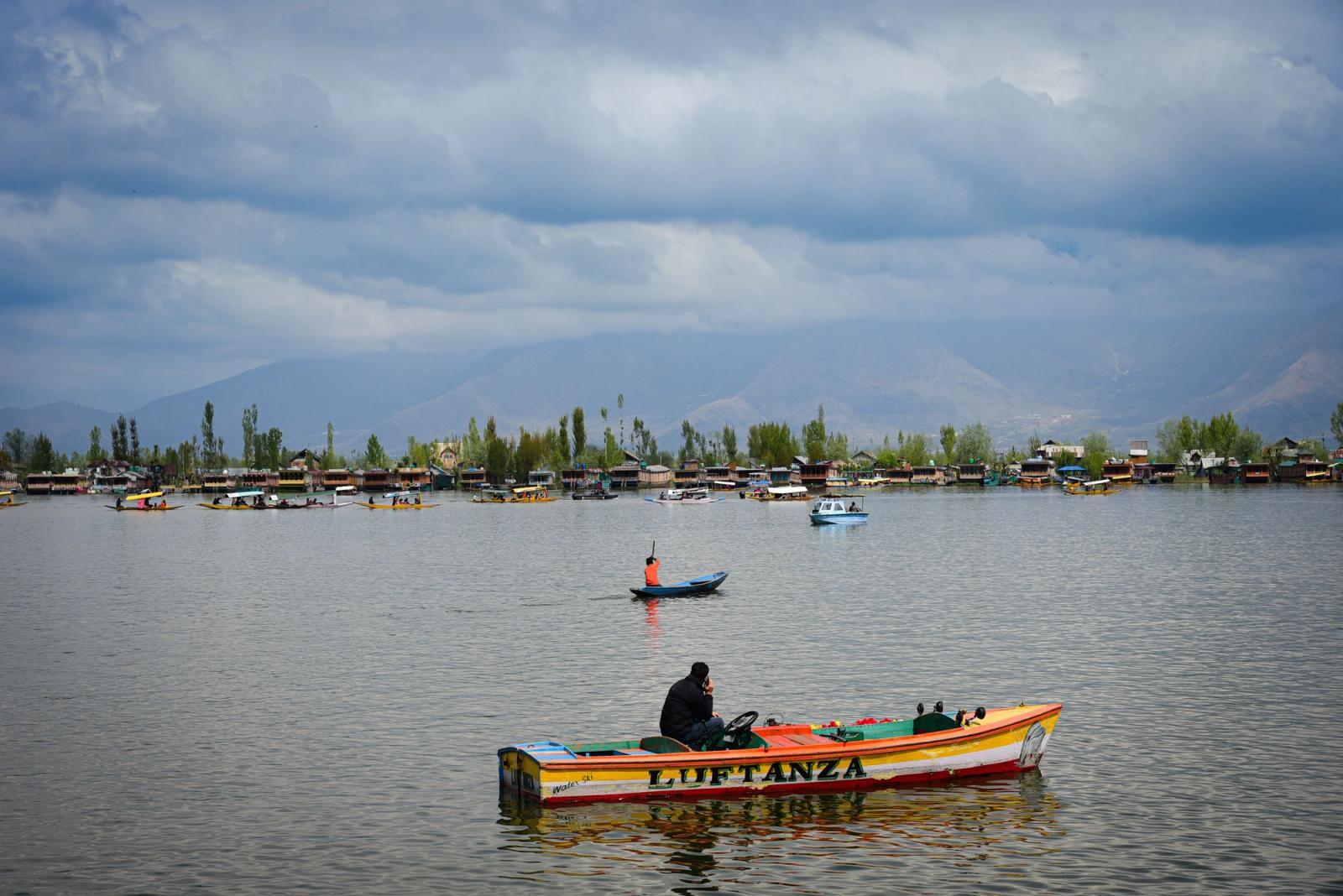 Tranquil scenery of Dal Lake in Srinagar with colorful boats and lush surroundings under a cloudy sky
