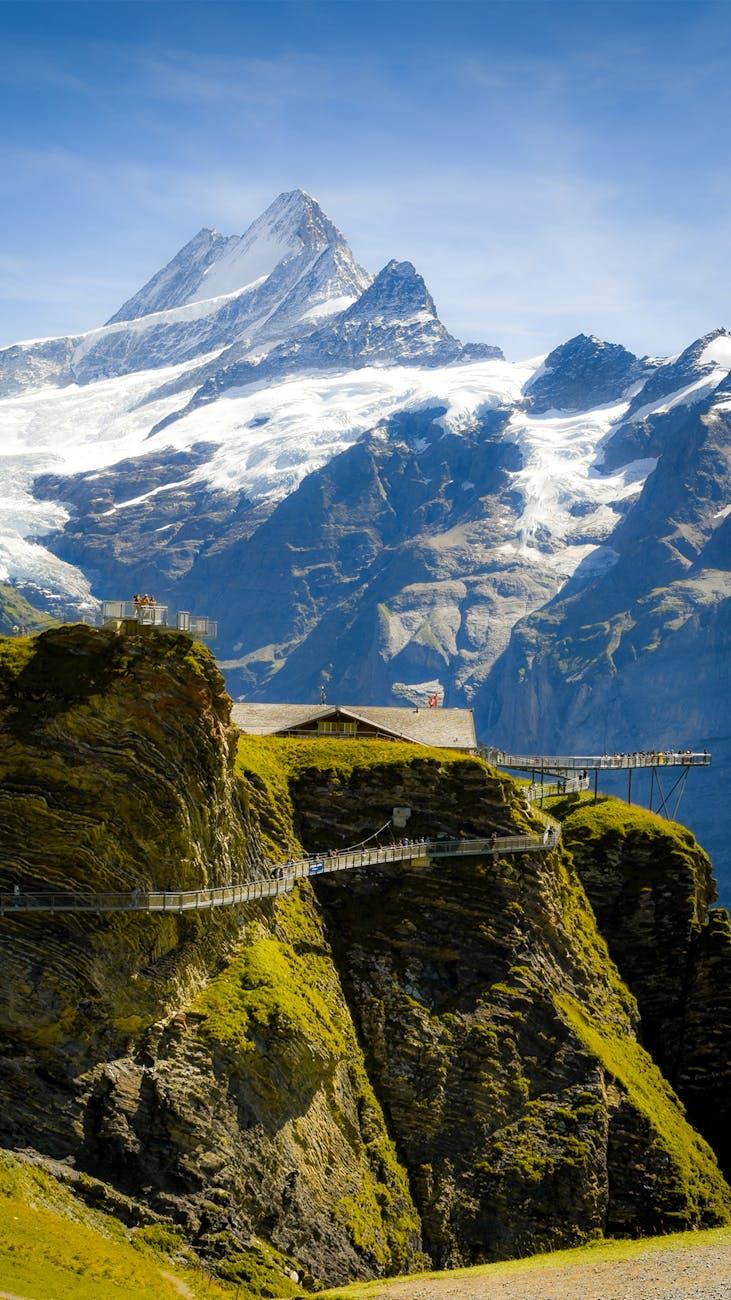Suspension walkway along a cliff edge facing jagged glaciated peaks