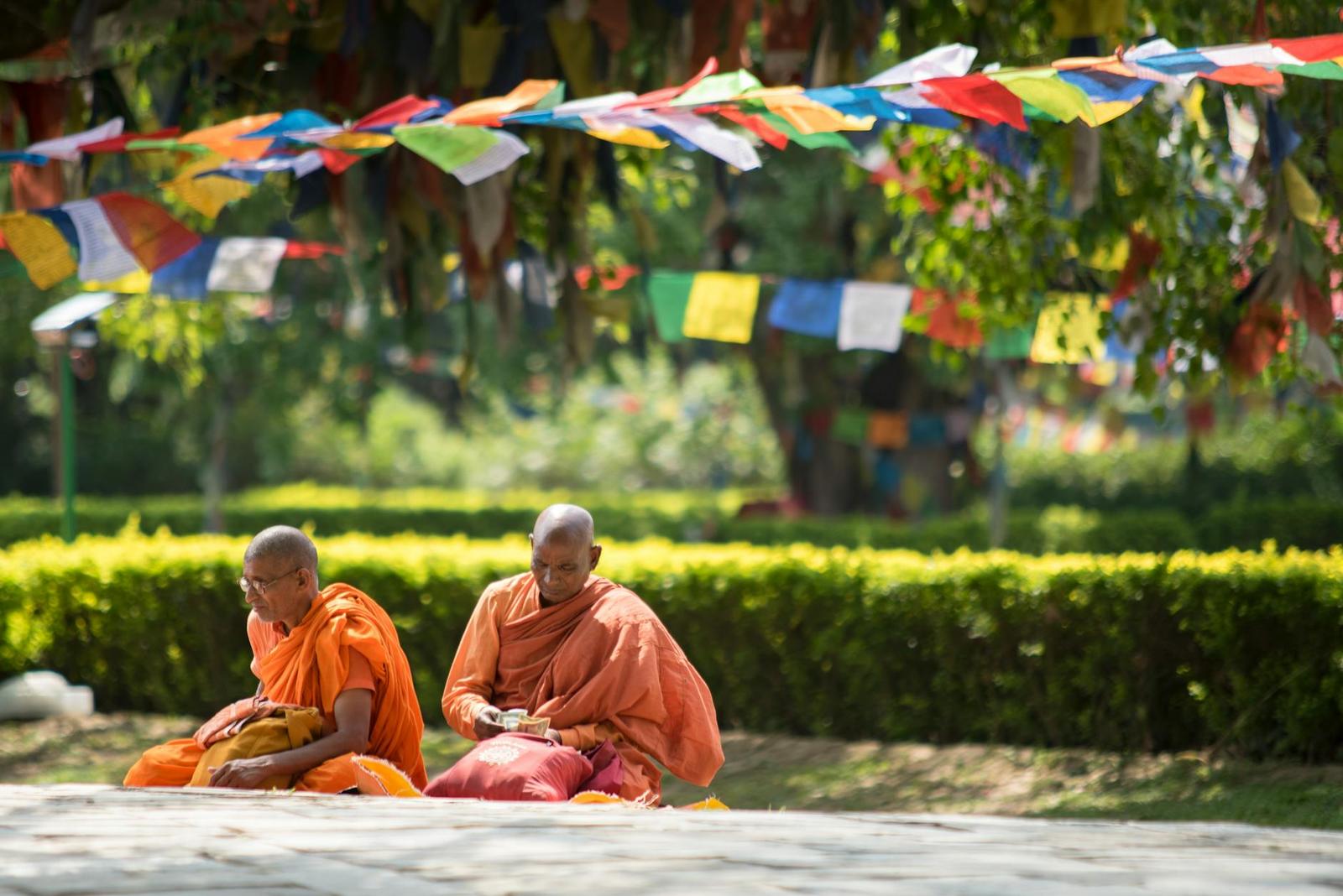 Two monks in orange robes sitting on the ground beneath strings of prayer flags