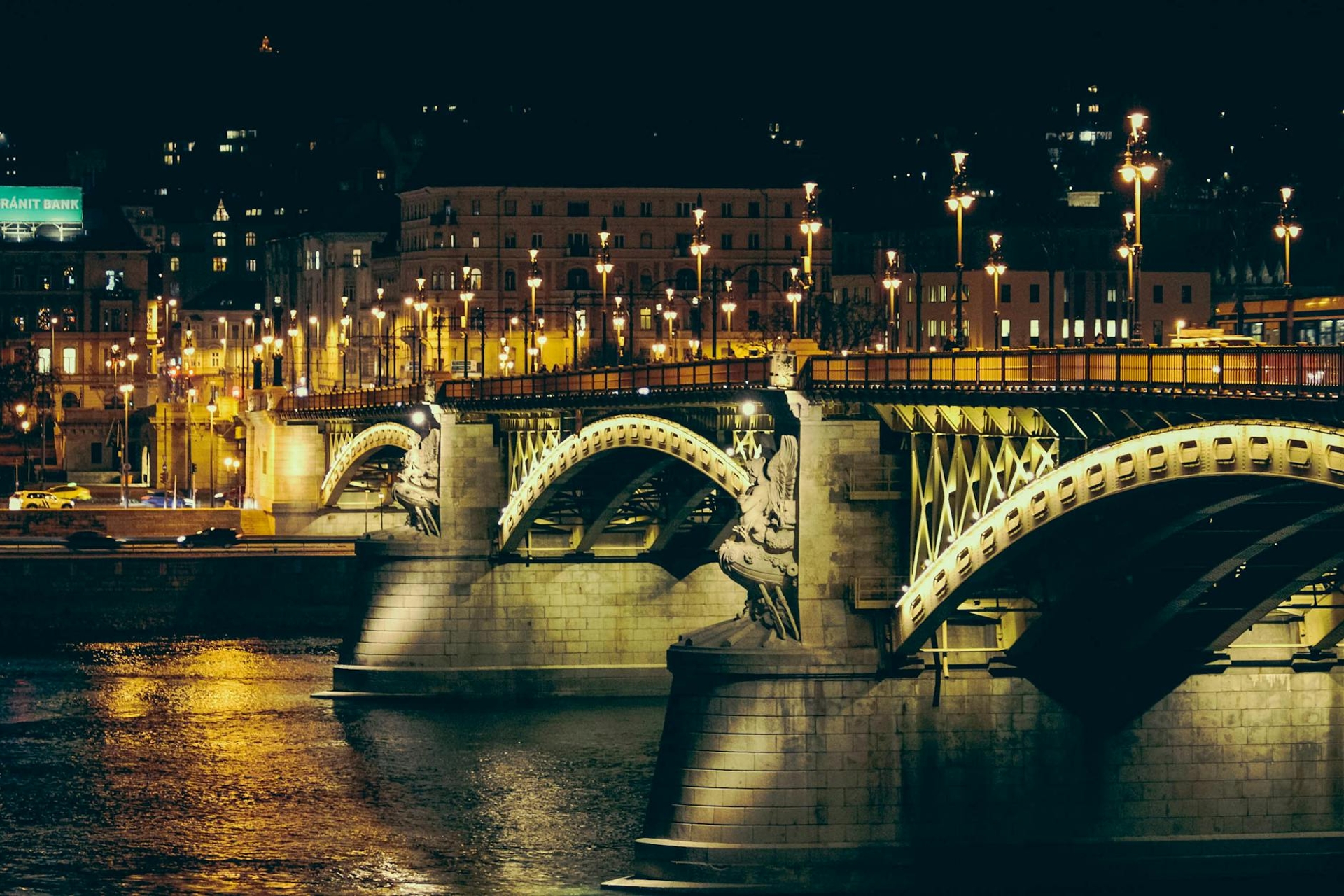 An ornate stone arch bridge lit up at night over a dark river