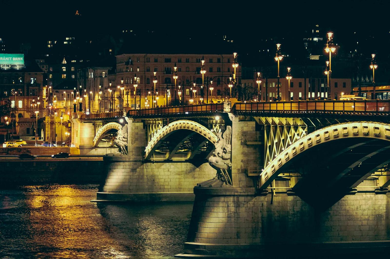 An ornate stone arch bridge lit up at night over a dark river