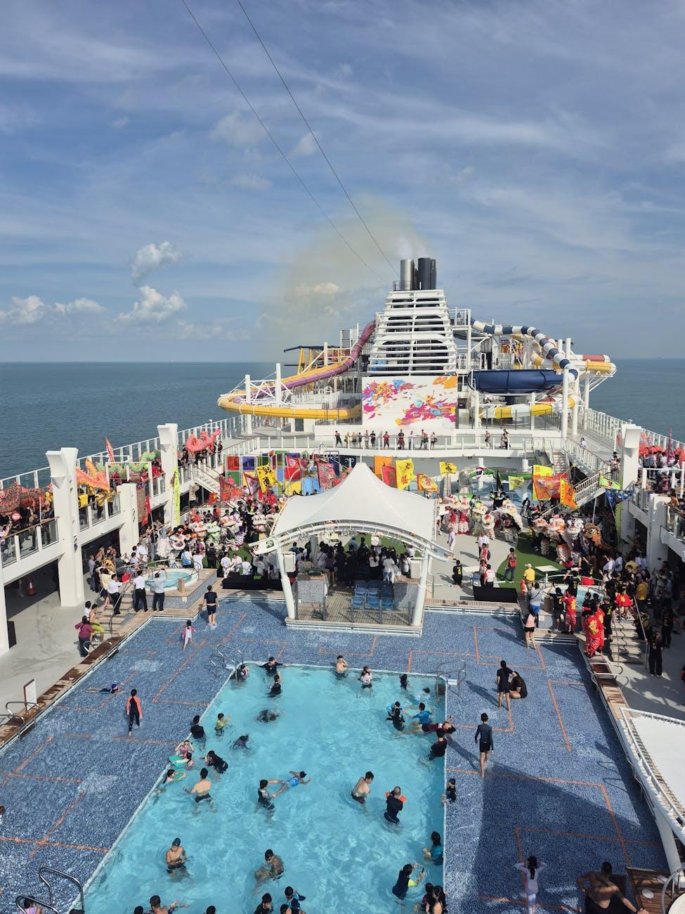 Crowded cruise ship pool deck with waterslides and towering funnel above