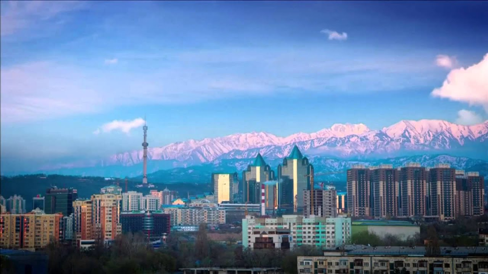A glass-towered city skyline below snow-capped mountains at dusk