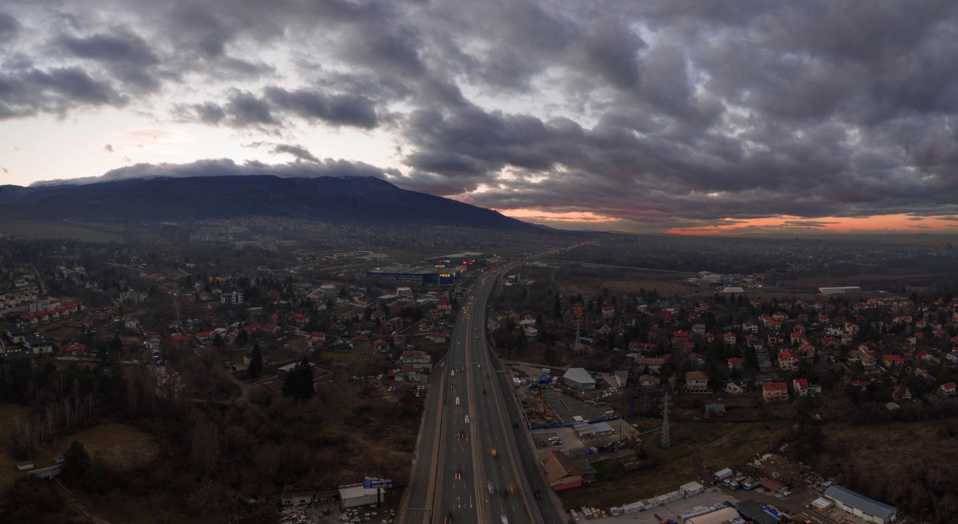 Aerial photograph of Sofia, Bulgaria with a highway, cityscape, and dramatic cloudy sky at sunset