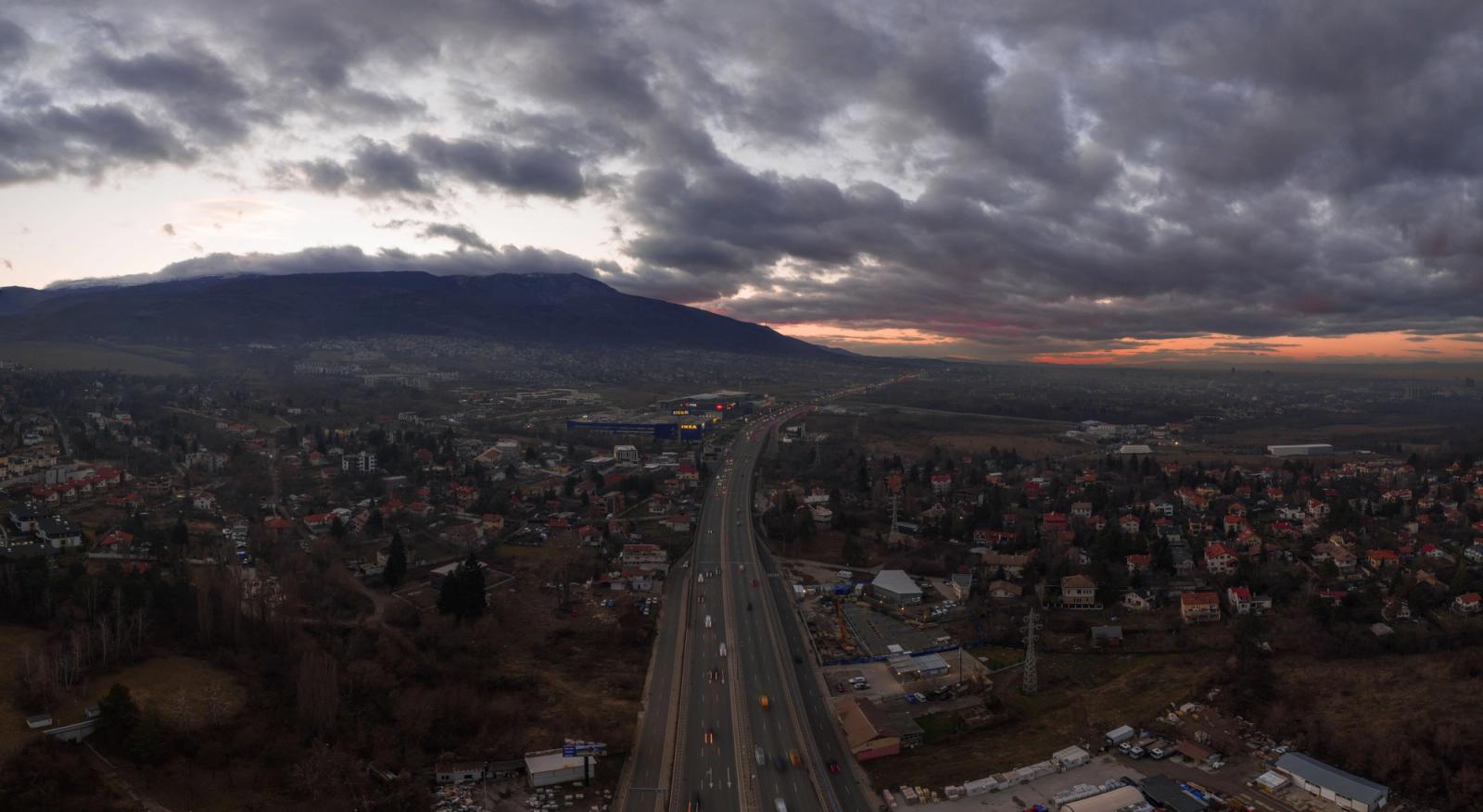 Aerial photograph of Sofia, Bulgaria with a highway, cityscape, and dramatic cloudy sky at sunset