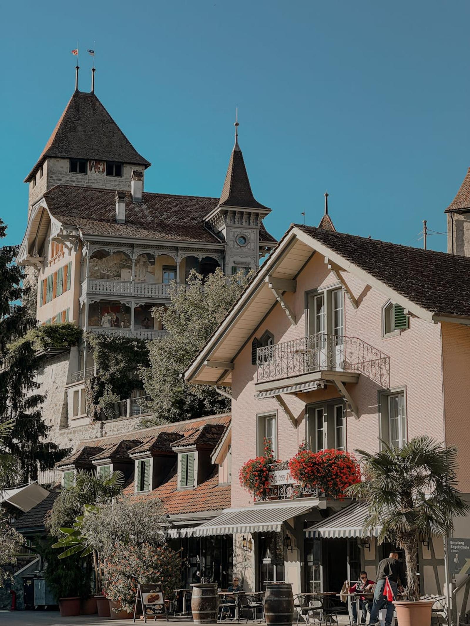 Turreted stone building beside a pastel cafe terrace under blue sky