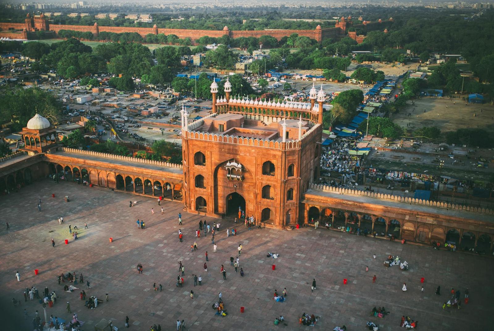 Aerial view of a red sandstone mosque gateway and a crowded courtyard