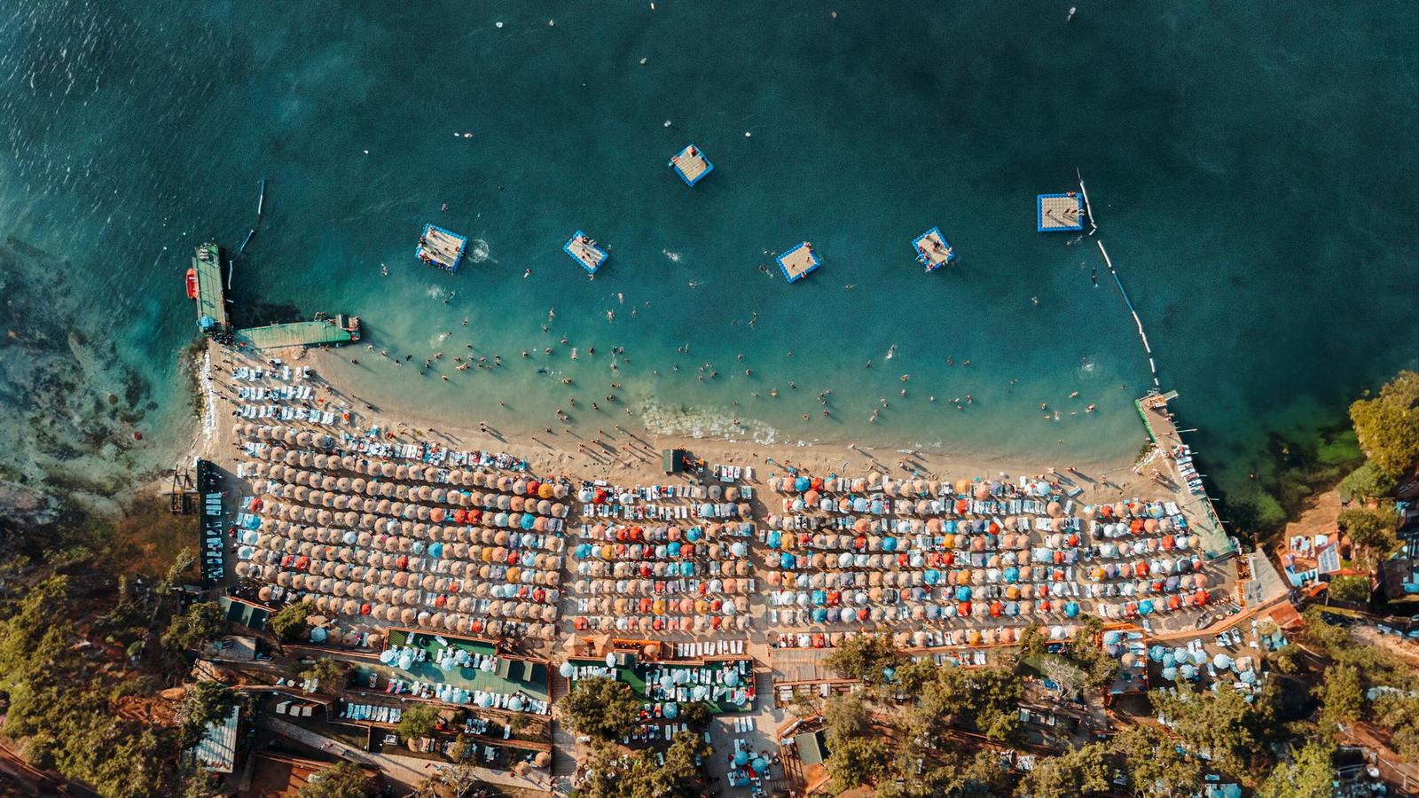 Aerial view of a packed beach lined with colourful umbrellas and boats