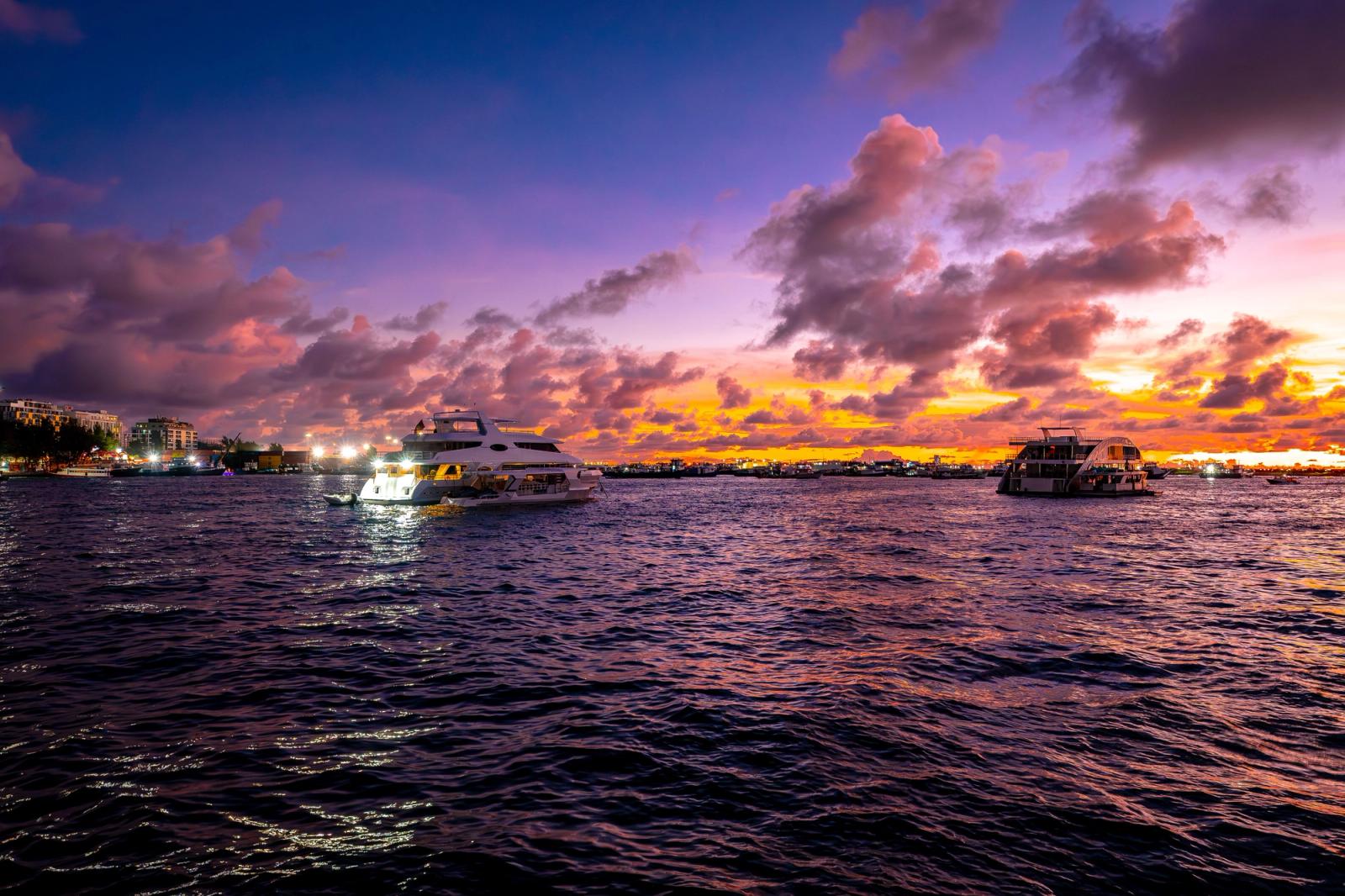 Boats on the water beneath a colourful sunset sky by a city harbour