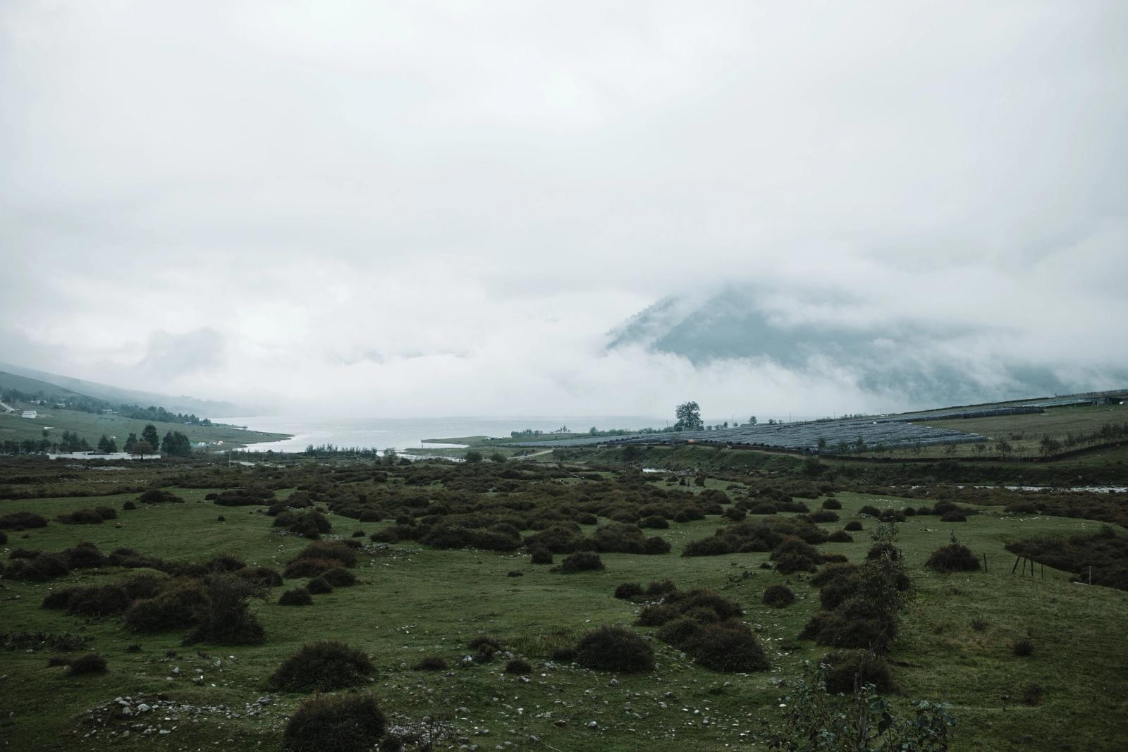 A tranquil valley landscape with misty clouds enveloping the mountains, offering a calm and scenic view