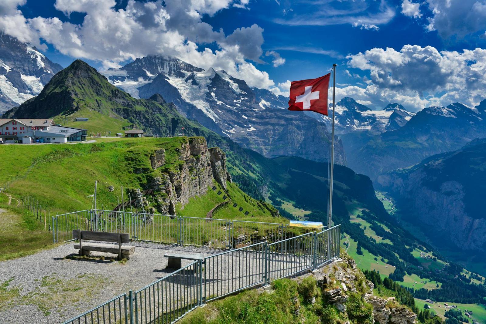 Swiss flag flying over a mountain viewpoint with a wooden bench