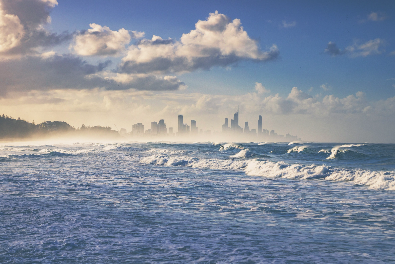 Beautiful ocean waves with the Gold Coast skyline in the background, under a partly cloudy sky