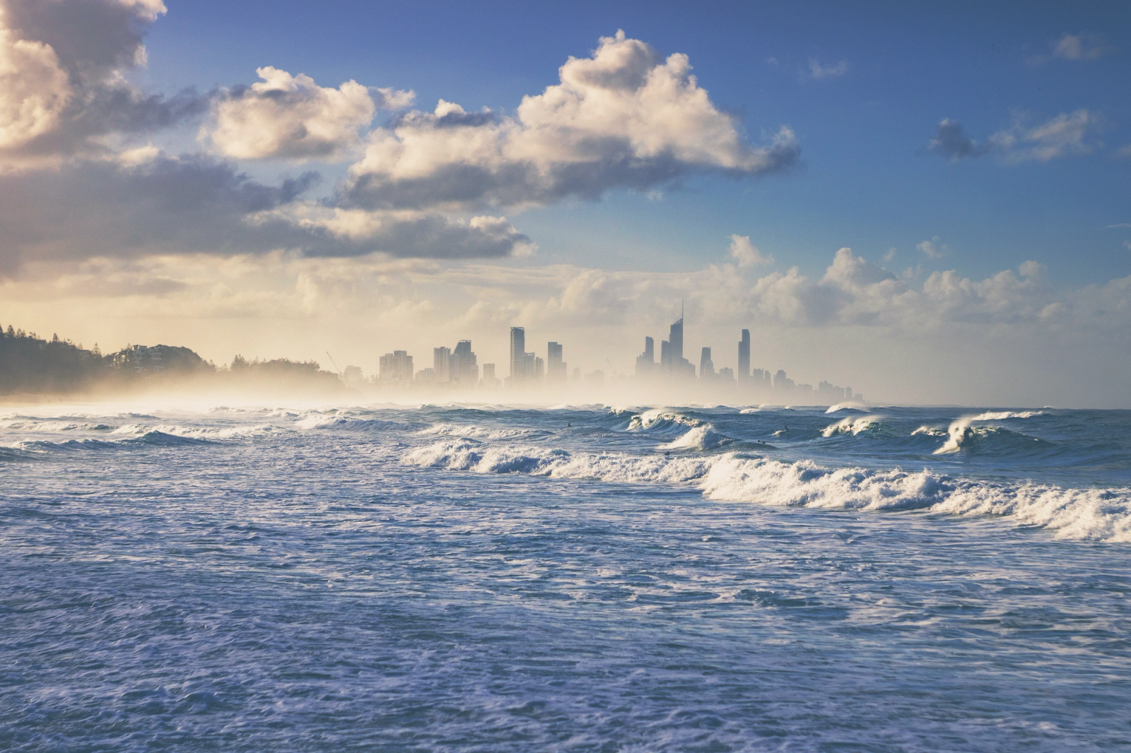 Beautiful ocean waves with the Gold Coast skyline in the background, under a partly cloudy sky