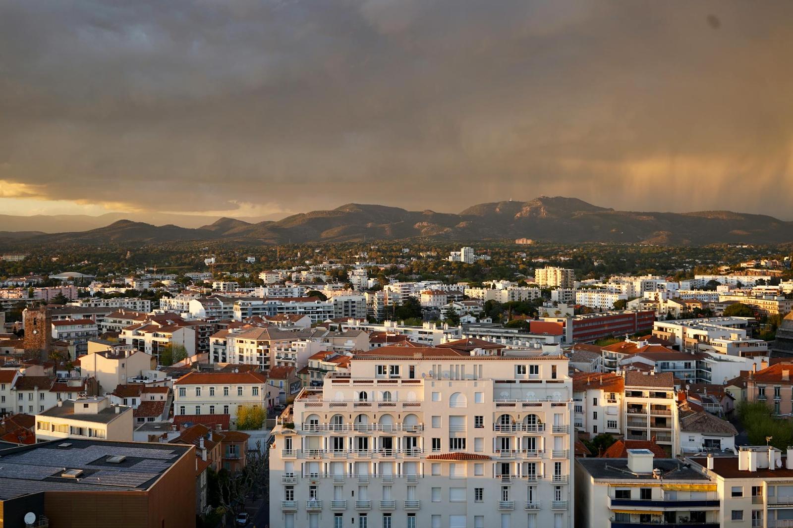Aerial view of a hillside city under a stormy, golden-lit sky
