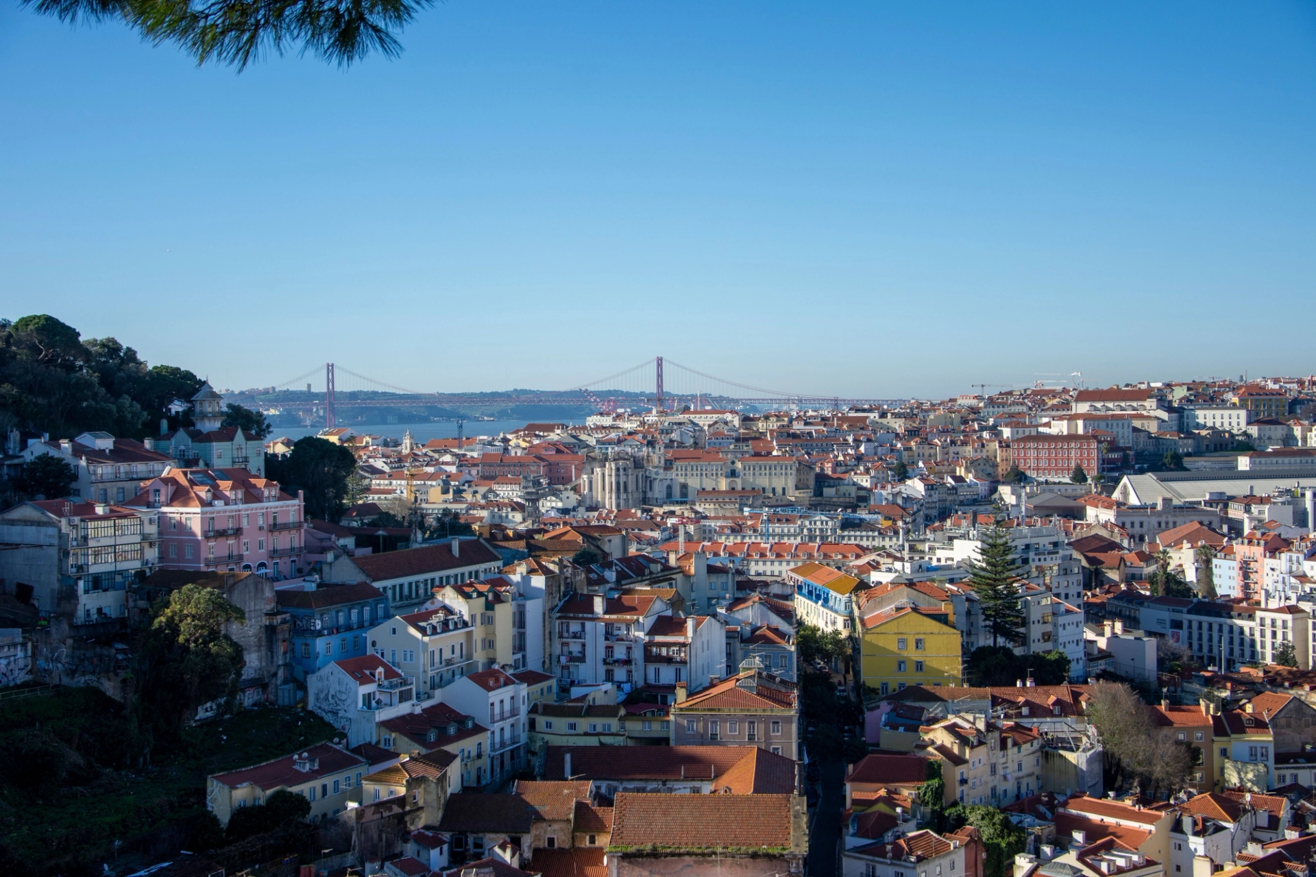 Aerial view of Lisbon, Portugal featuring the iconic 25 de Abril Bridge under a clear blue sky