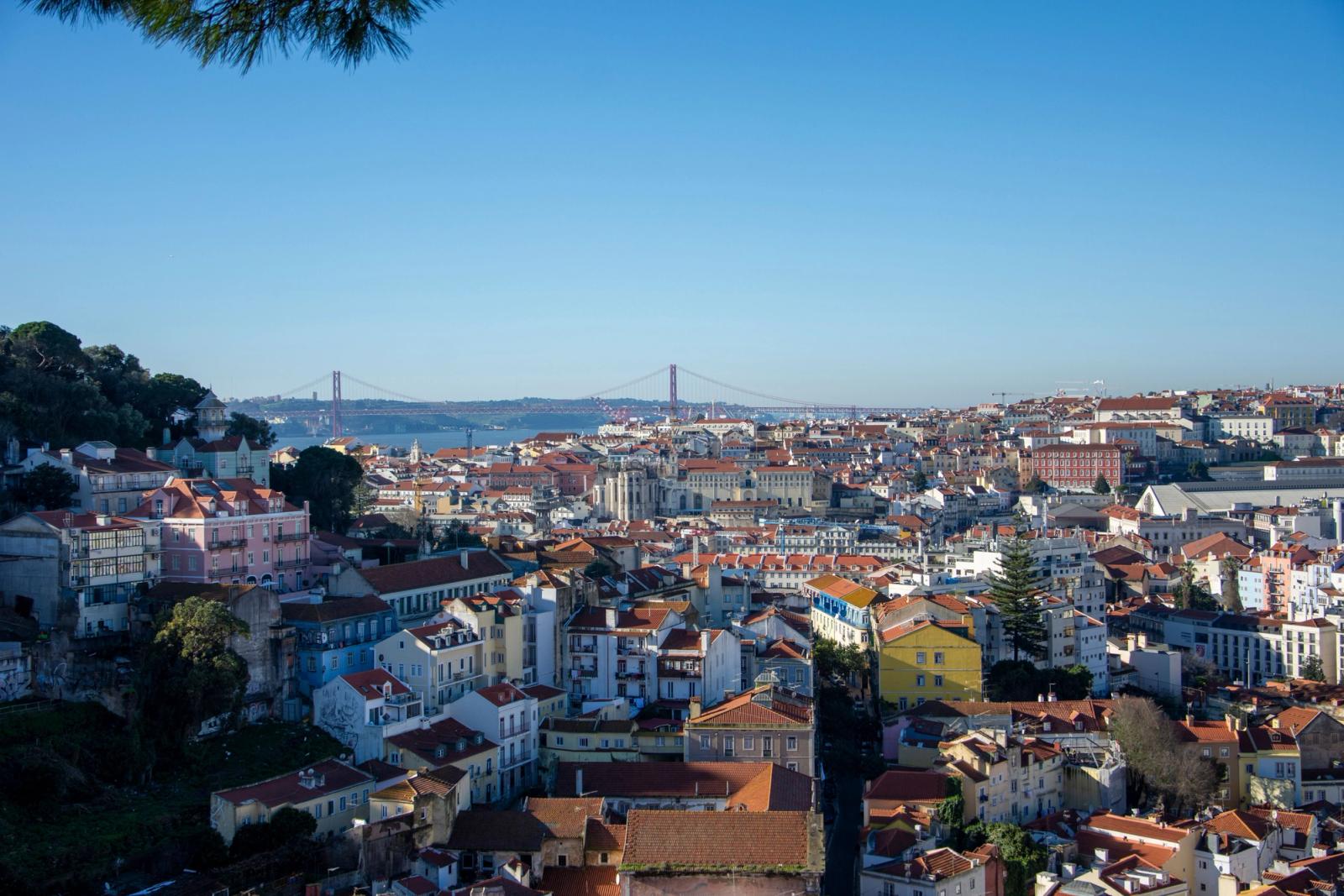 Aerial view of Lisbon, Portugal featuring the iconic 25 de Abril Bridge under a clear blue sky