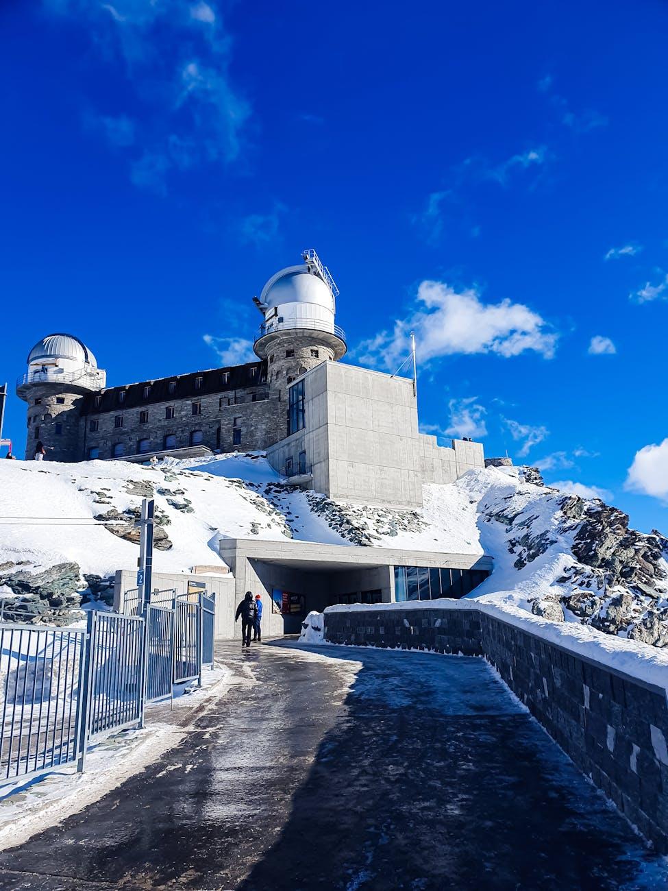 Visitors walking toward a stone observatory building on a snowy summit