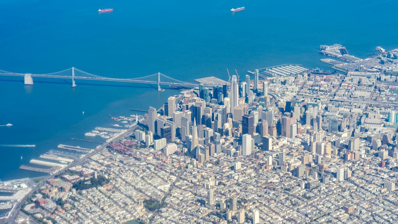 Aerial view of a dense waterfront city with a long suspension bridge