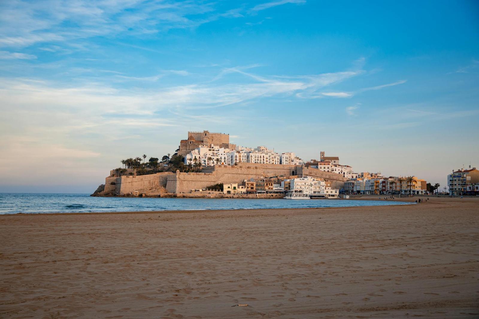 Serene landscape featuring Peñíscola Castle with a vast sandy beach and blue sky